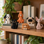 Three crochet dogs and three crochet cats sitting on a wooden bookshelf among books and houseplants.
