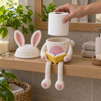 An adult hand lowers an upright white toilet roll above an empty Bunny cup while the pink-lined ear cap rests beside it.