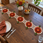 A long crochet table runner with five layered copper flowers and olive leaves on five cream round lace bases joined by four openwork bridges, on a set wooden dining table.