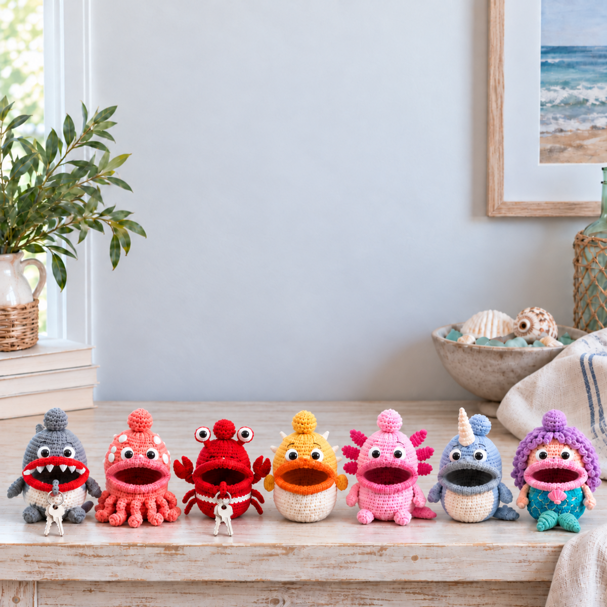 Crochet key pouches Shark, Octopus, Crab, Pufferfish, Axolotl, Narwhal, Mermaid stand on a pale wooden shelf beside a bowl of seashells.