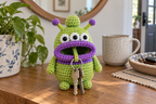 Lime Alien crochet key pouch with three eyes, purple-tipped antennae, a purple band and a purple rolled lip, with house keys hanging from its open mouth.
