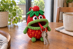 Red Strawberry crochet key pouch with a green leaf crown, yellow body seeds and green limbs and rolled lip, with house keys hanging from its open mouth.