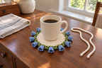 Bluebell: a coffee mug on a flat warm-white crochet coaster edged with small blue bells and green leaves.