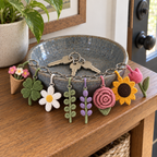 Eight crochet flower and leaf keychains around a ceramic key dish on a wooden console by the door.