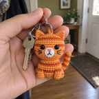 A small orange striped crochet cat keychain with house keys held in an adult hand.