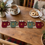 Five alternating burgundy and sage cocoa mug motifs with gold stars and cream marshmallows joined as a crochet runner on a kitchen table beside tea and biscuits.