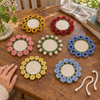 Seven empty flat Flower Bouquet crochet coasters with white centres and green leaf rings on a wooden table: Sunflower, Poppy, Carnation, Lily of the Valley, Cornflower, Buttercup, Hydrangea.