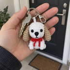 White crochet puppy with tan floppy ears and a red neck bow hanging beside house keys in an adult hand.