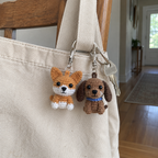 Orange-and-white corgi and brown dachshund crochet keychains clipped to a canvas tote strap beside a house key.