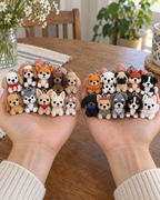 Two adult hands each holding ten different crocheted dog keychains, showing all twenty dog designs.