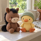 A brown crochet horse and yellow duckling in a sage bonnet sit together on a sunny windowsill beside a potted herb.