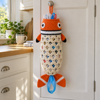 An orange clownfish bag holder hangs on a pantry door knob, with a black-edged white head band, cream mesh and white-banded orange tail lobes.