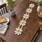 The ivory Daisy Meadow runner with yellow centres, sage leaves and cream lace joins lies on a dark wooden breakfast table beside a blue mug and toast.