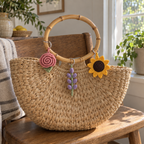 Rose, lavender and sunflower crochet keychains on the bamboo handle of a straw bag.