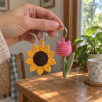 An adult hand holding sunflower and tulip crochet keychains by their rings.