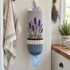A pale-grey crochet holder with purple lavender spikes, grey-green stems, a whitewashed rim and a grey-blue pot hangs beside a linen tea towel and dried lavender.
