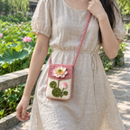 A dusty-pink and cream Lotus crochet phone pouch worn crossbody over a linen dress beside a lotus pond.