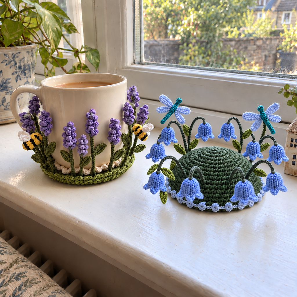 An olive-green lavender coaster hugging a cream mug of tea beside a forest-green domed bluebell coaster with dragonflies on a sunny windowsill.
