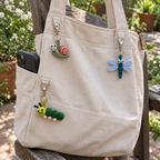 Finished crochet garden bug charms hanging from a canvas bag in a garden.