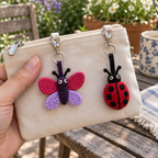 Close view of a pink-and-lilac crochet butterfly and red spotted ladybug, showing cotton stitches.