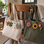 Eight small crochet flower and leaf keychains hang from linen and olive canvas bags on a wooden chair beside a set of house keys.