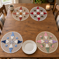 Four seasonal gnome crochet doilies at the far and near ends of a wooden dining table, with a mug and candle at the back, a white dinner plate in front and bare wood between the rows.