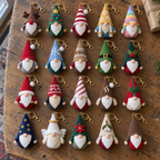 Twenty distinct Christmas gnome keychains with colourful decorated hats laid out in four rows on a wooden table.