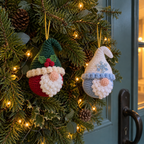 Holly and Snow gnome baubles hang on an evergreen wreath on a blue-green front door.