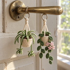 Miniature crochet hanging-basket plants suspended from a door handle, with cotton stitches and cream hanger cords visible.