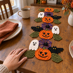 An adult left hand gently touching an olive crochet leaf beside an orange pumpkin in the finished Halloween runner on a wooden table with plates and a coffee mug.