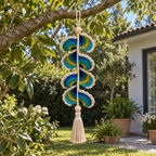 A blue, teal, green and gold Peacock Fan crochet wind spinner hanging by its oatmeal loop from a tree branch in a home garden.