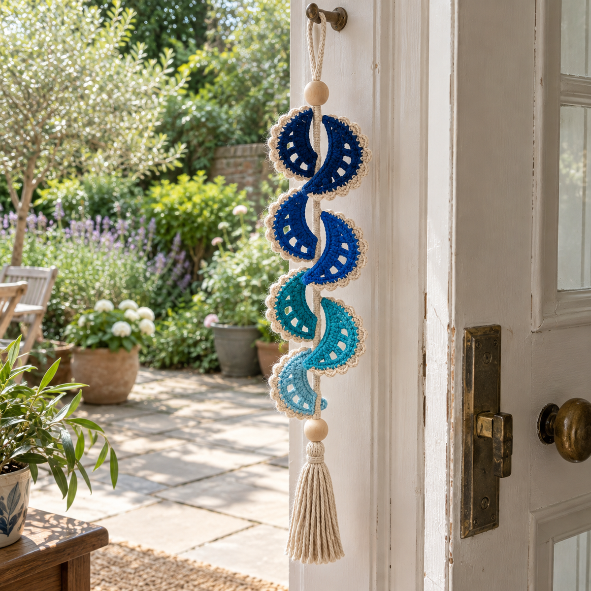 A navy, cobalt, teal and aqua Sapphire Crescent crochet wind spinner hanging beside an open garden door.
