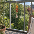 A mustard, amber, terracotta, rust and olive Amber Diamond crochet wind spinner hanging by its oatmeal loop from a balcony rail.