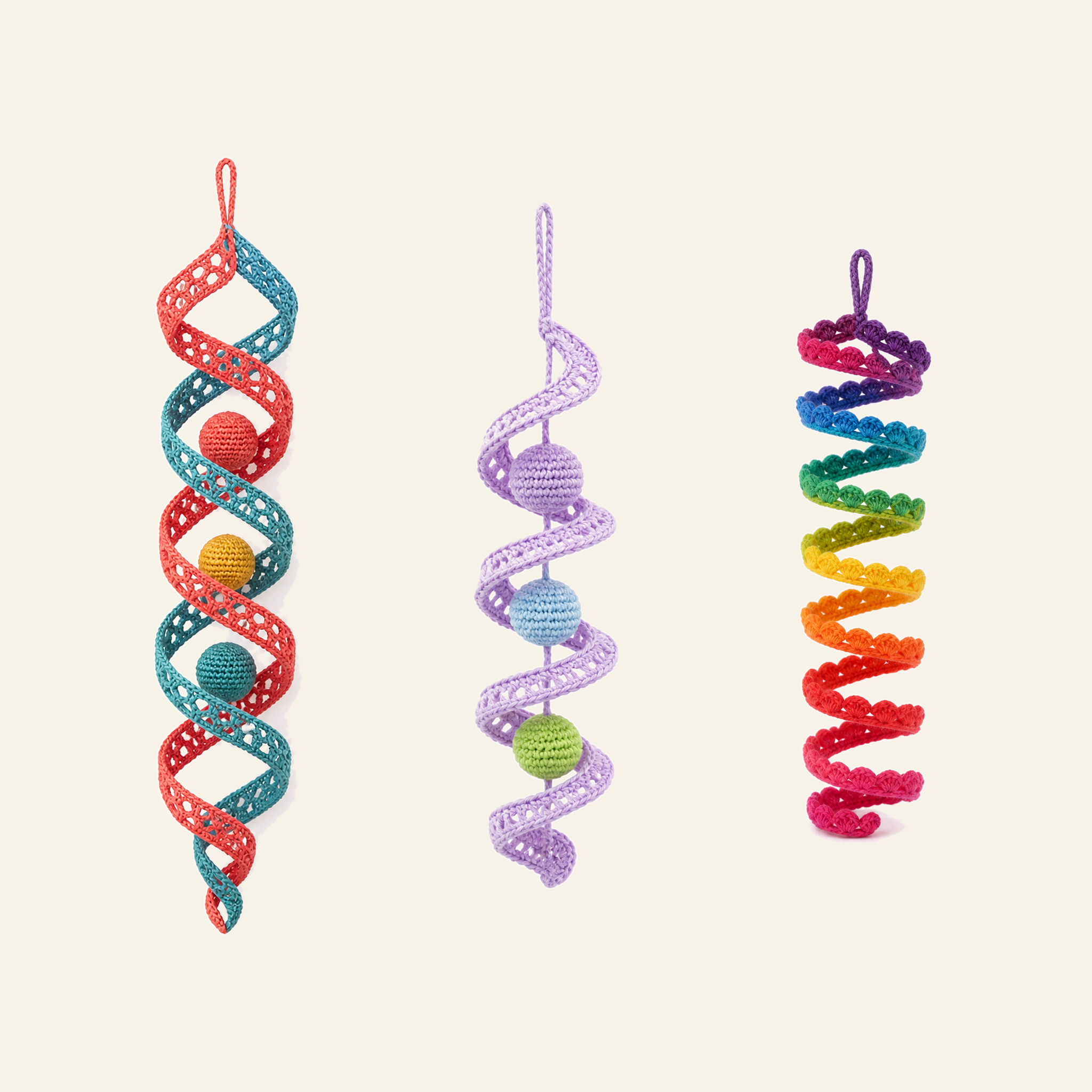 Three crochet lace wind spinners side by side: a coral and teal double helix, a lilac spiral with three balls hanging inside it, and a rainbow coil edged with scalloped shells, every band openwork