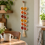 Six pairs of gold, orange, and rust crochet fans with cream edging hang from a cream cord beside a breakfast nook window.