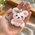 White Rose Bear with a pink rose, green calyx, pink bow and two pearl-ended chains held in an adult palm beside a house key.