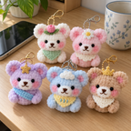 Tulip, Daisy, Star, Cloud and Crown crochet bear keychains on a home desk beside a mug and phone.