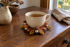 Autumn Forest crochet mushroom coaster: rust base, brown edge, plain brown and orange caps, four ochre oak leaves, with a cup set on it, the mushrooms standing up round its foot.
