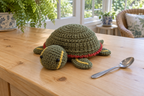 Painted Turtle pop-up crochet turtle coaster, an olive shell with a red edge and yellow stripes, shown with no cup, a rounded domed shell with its head and feet resting.