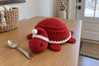 Santa Turtle pop-up crochet turtle coaster, a red shell with a white edge and a soft Santa hat, shown with no cup, a rounded domed shell with its head and feet resting.