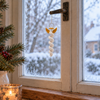 An ivory crochet spiral angel with gold wings and a gold halo hanging by a thread from a window handle in front of frosty glass.