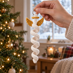 An adult hand holding an ivory crochet spiral angel with gold wings and a gold halo by its silver hanging ring.