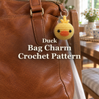 Yellow crochet duck charm with an orange beak hanging from a brown leather handbag beside a wooden chair, with the title Duck Bag Charm Crochet Pattern.