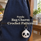 A small white and black crochet panda charm hangs from the zipper of a navy bag on a wooden kitchen chair, with the title Panda Bag Charm Crochet Pattern.