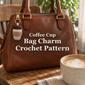Cream crochet coffee-cup bag charm with a kraft tan sleeve and brown tiered lid hanging from a silver ring on a brown leather handbag beside a coffee mug.