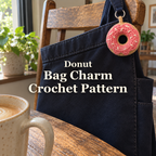 A tan crochet donut with pink glaze and white sprinkles hanging from a navy canvas bag beside a wooden chair and coffee mug.