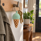 Mint crochet ice cream cone charm and two brass house keys hanging from a silver ring on a wooden entryway rail.