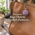 Lilac crochet macaron with a cream filling hanging from a tan leather bag zipper beside a window, with the title Macaron Bag Charm Crochet Pattern.