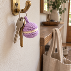 Lilac and cream crochet macaron hanging beside two house keys from a silver ring on a brass hallway hook.
