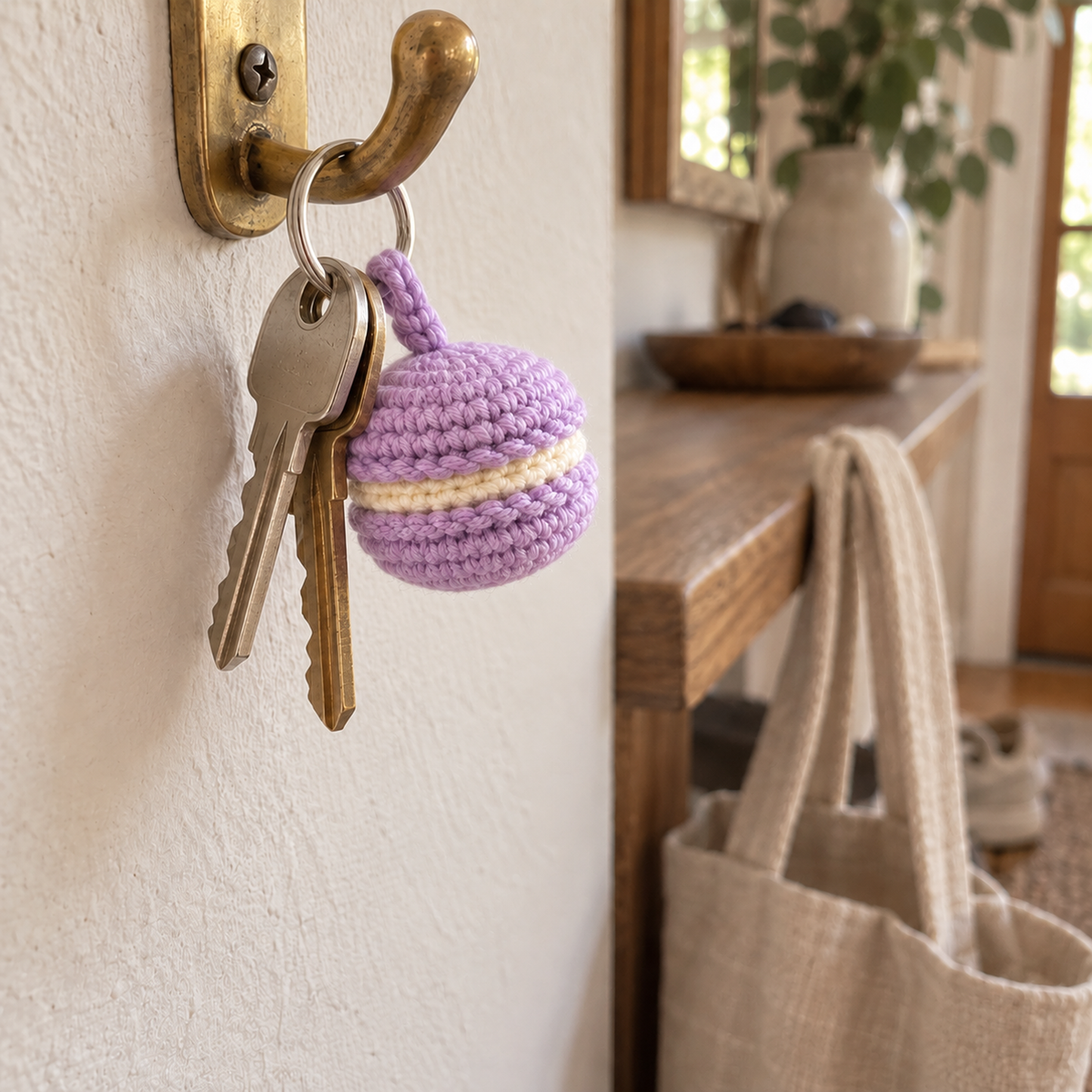 Lilac and cream crochet macaron hanging beside two house keys from a silver ring on a brass hallway hook.